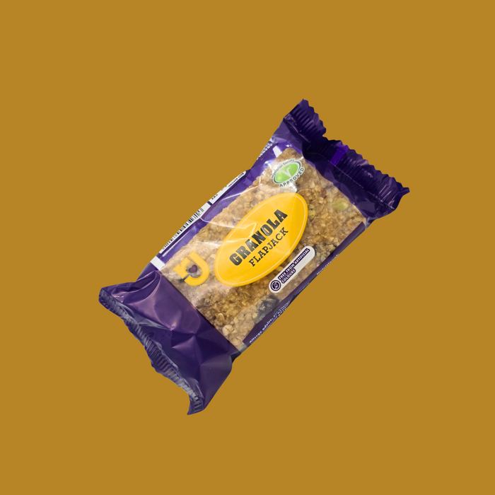 Hand holding a granola flapjack bar over a backpack on a hiking trail

