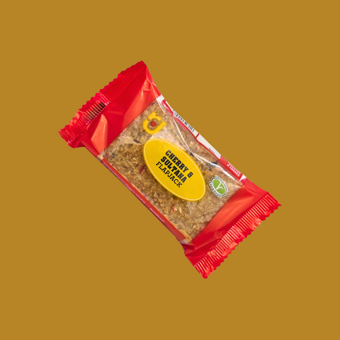 Hand holding a Cherry & Sultana flapjack over a picnic blanket

